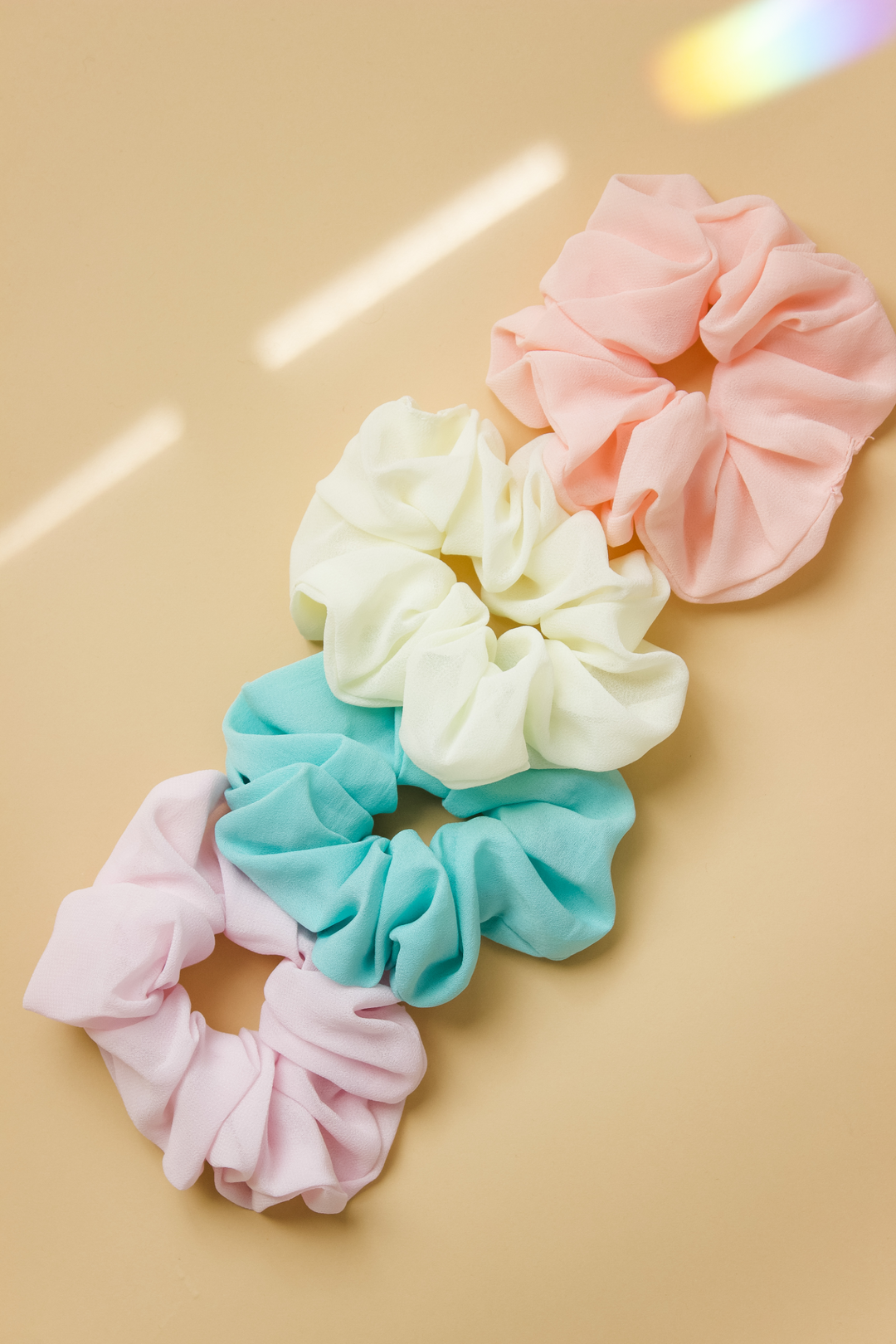 Line up of pastel colored chiffon scrunchies in peach, pale yellow, aqua, and light purple